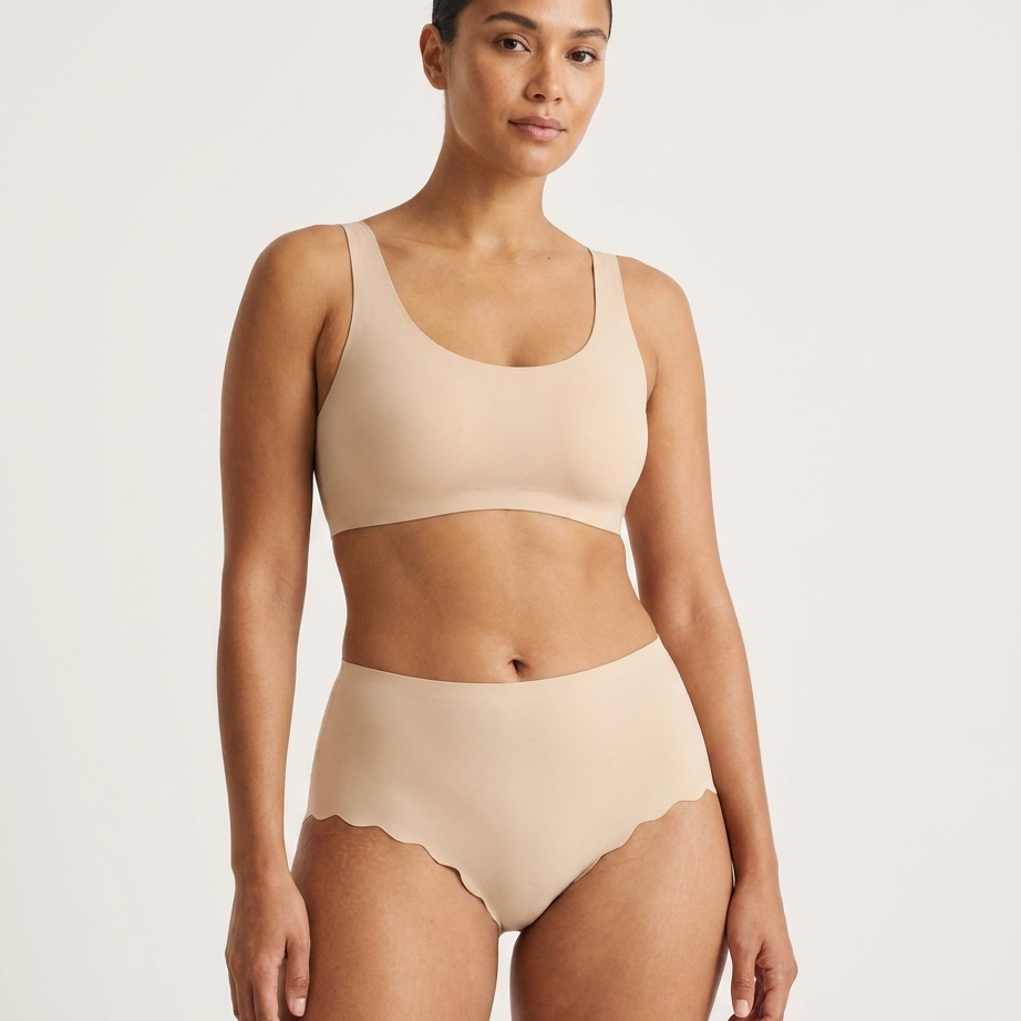 Woman wearing beige Invisible Edge Scalloped Briefs against a plain background