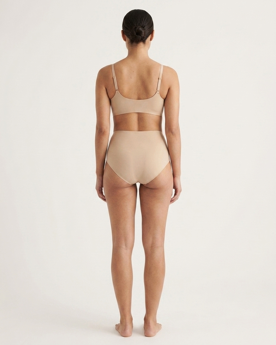 Backside of a woman wearing beige Invisible Edge Scalloped Briefs against a plain background