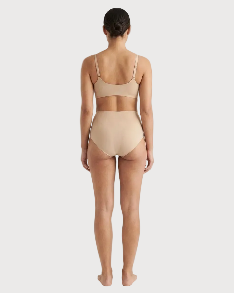 Backside of a woman wearing beige Invisible Edge Scalloped Briefs against a plain background