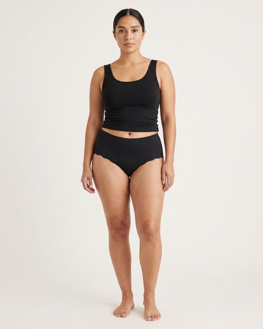 Woman wearing black Invisible Edge Scalloped Briefs against a plain background