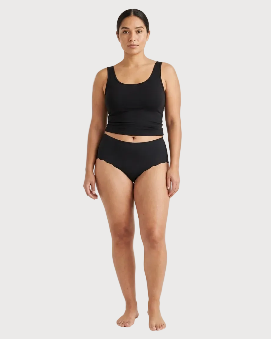 Woman wearing black Invisible Edge Scalloped Briefs against a plain background