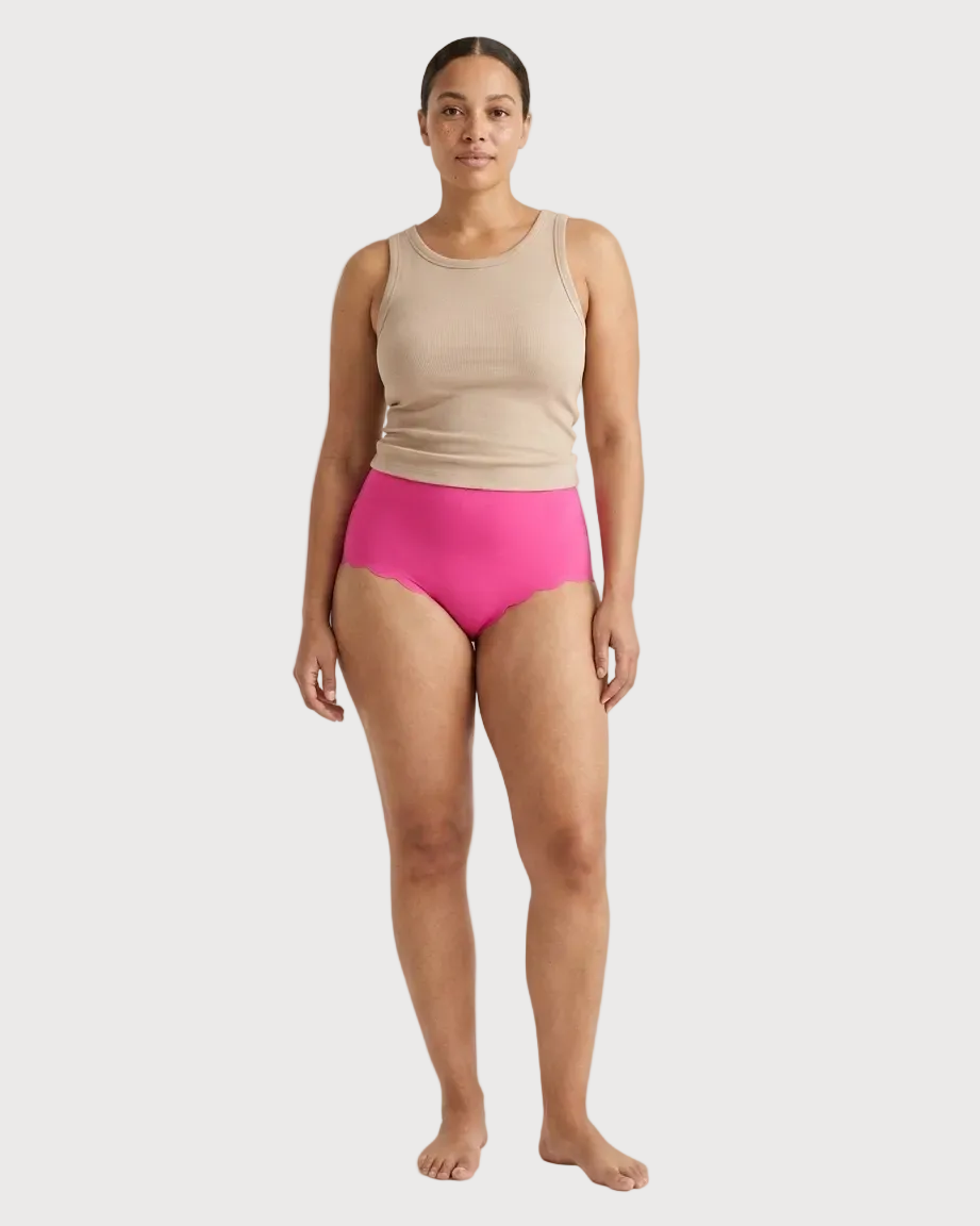 Woman wearing pink Invisible Edge Scalloped Briefs against a plain background