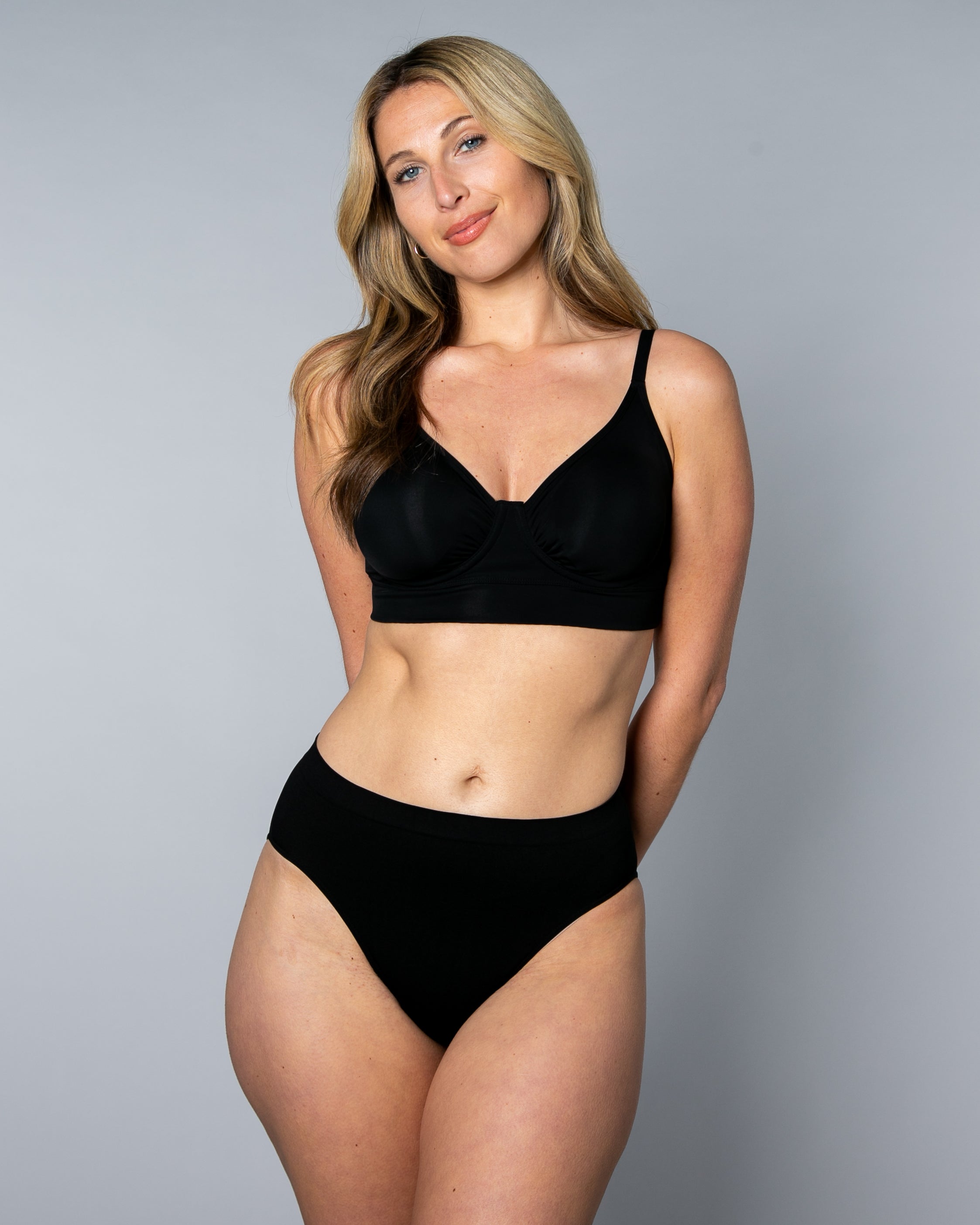 Woman wearing a black No Wire Underwire bra and panties set against a gray background