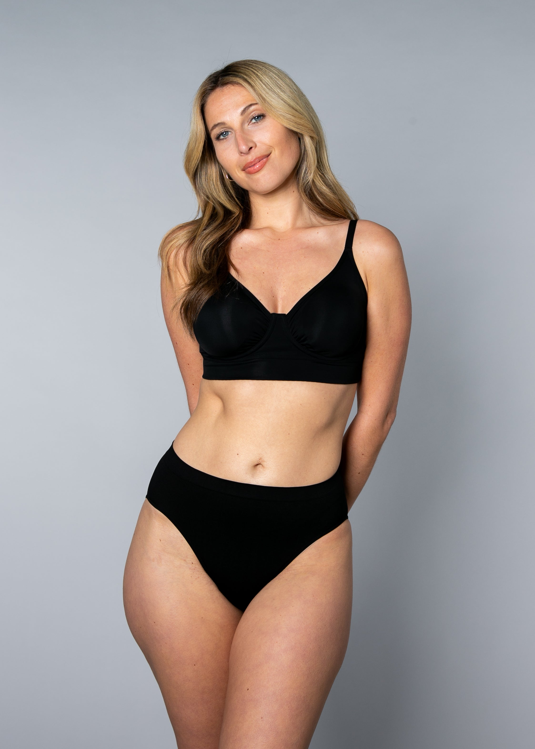 Woman wearing a black No Wire Underwire bra and panties set against a gray background