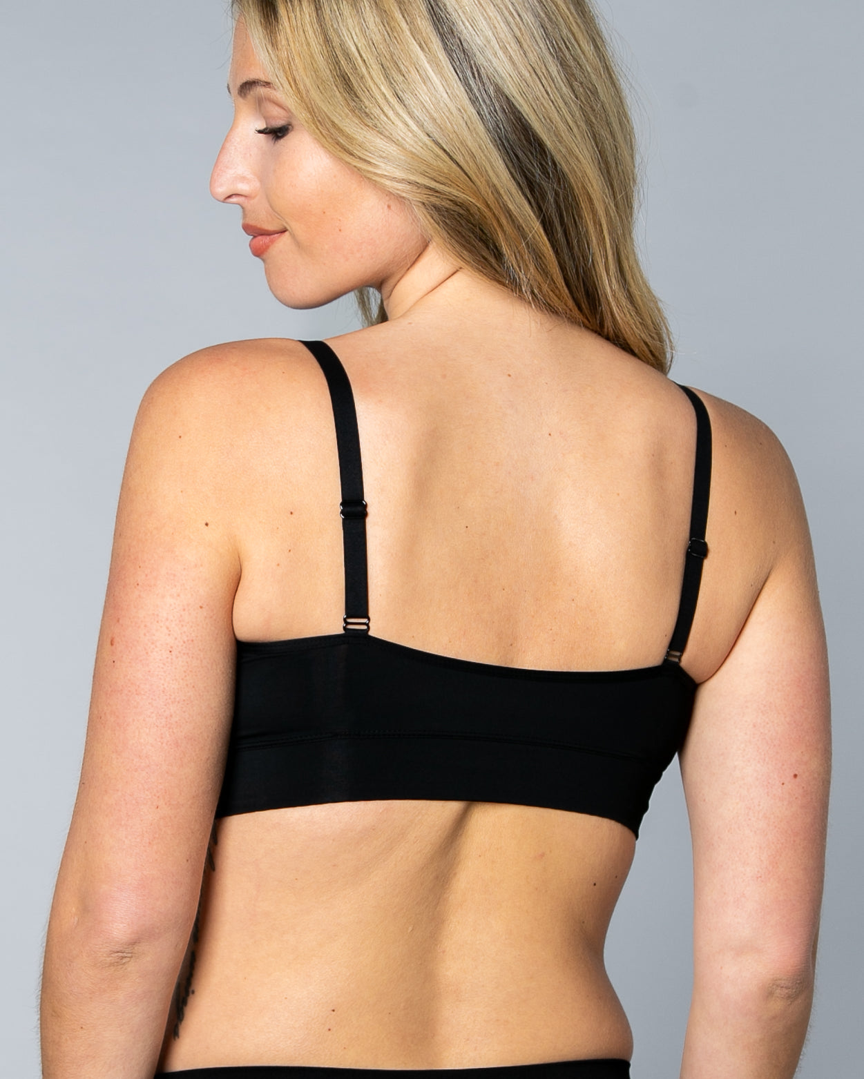 Back view of a woman wearing a black No Wire Underwire bra and panties set against a gray background