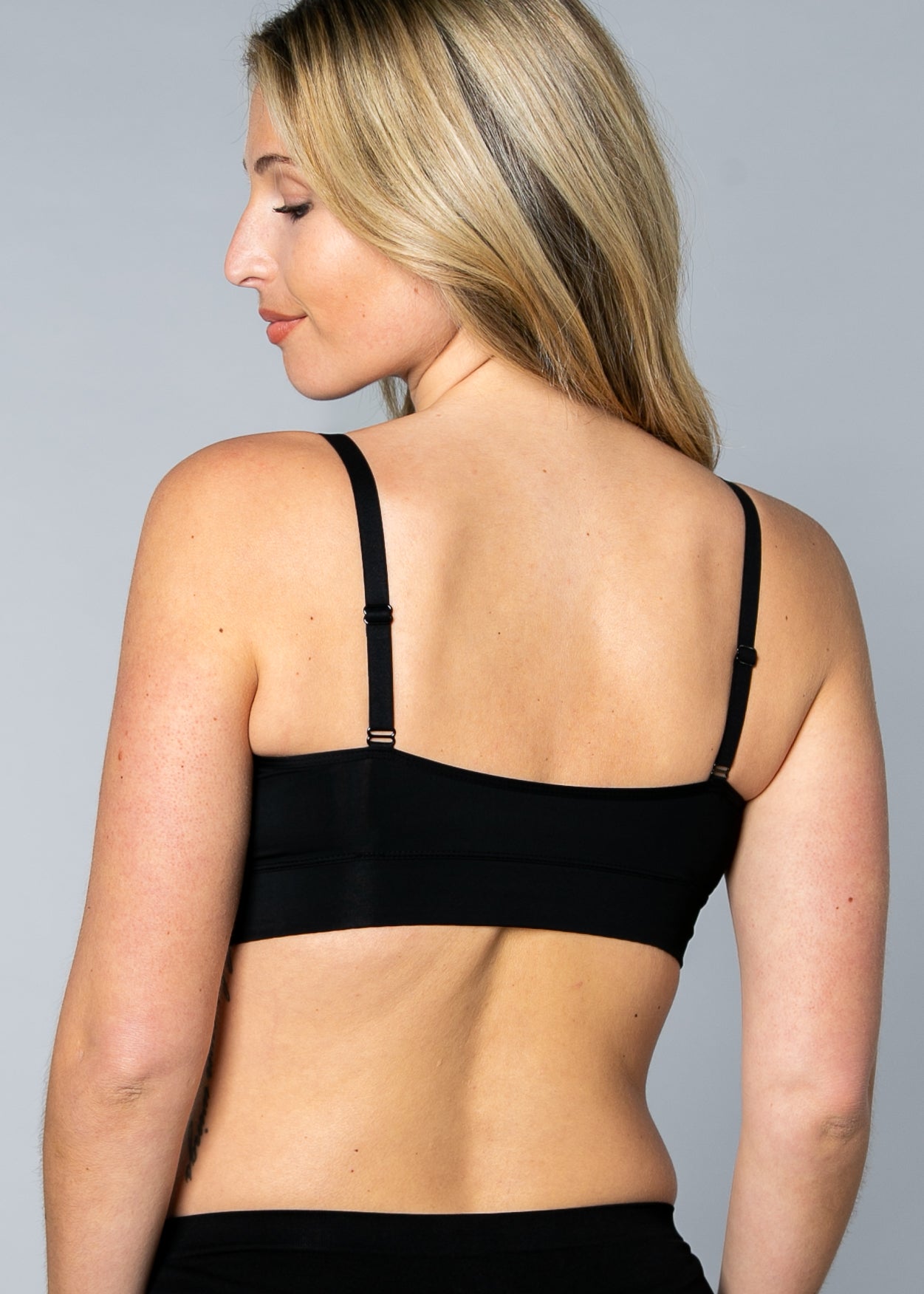 Back view of a woman wearing a black No Wire Underwire bra and panties set against a gray background