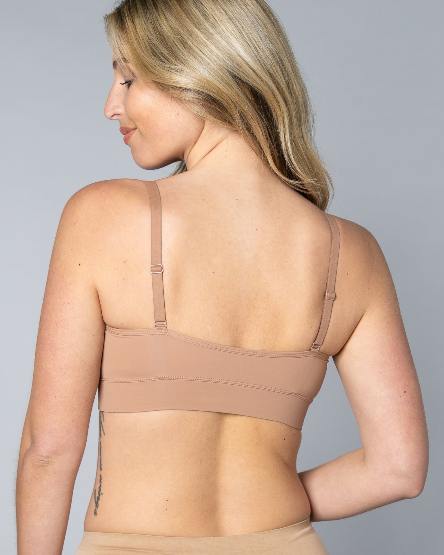 Back view of a woman wearing a beige Butterknit No Wire Underwire bra and underwear set against a gray background