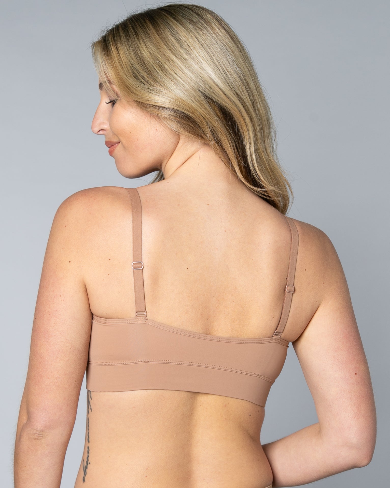 Back view of a woman wearing a beige Butterknit No Wire Underwire bra and underwear set against a gray background