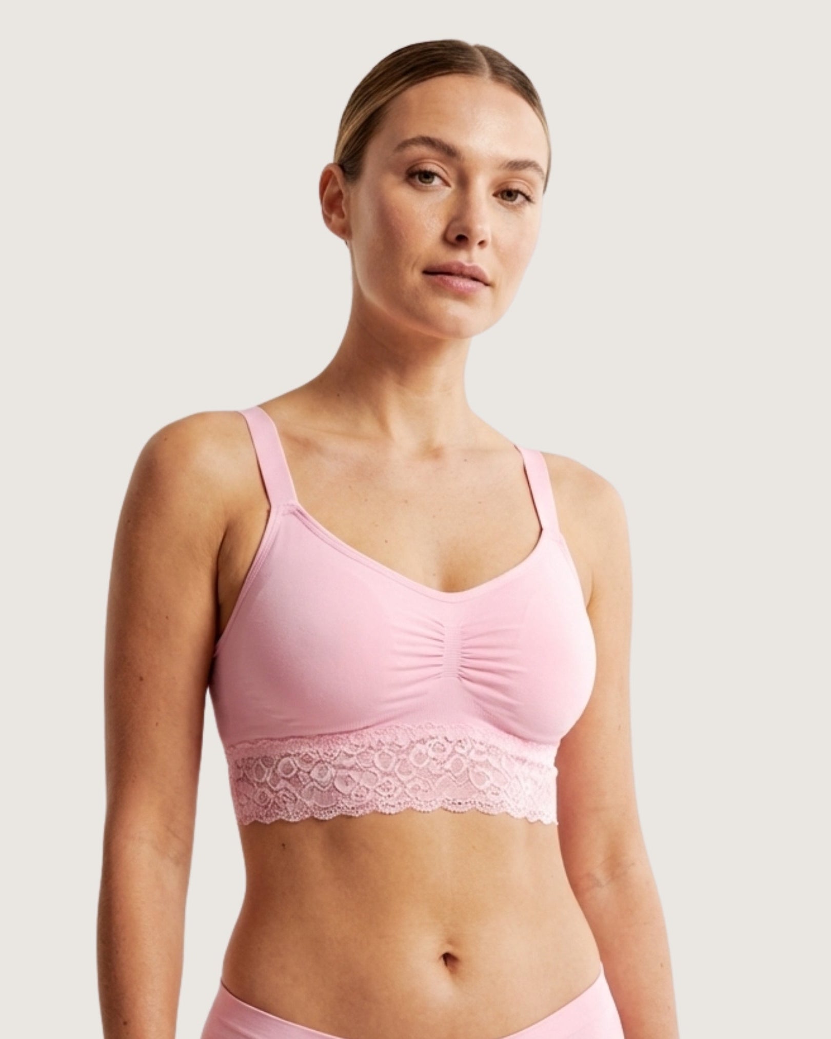 Woman wearing a pink Seamless Bra with lace Band with lace trim on a plain background
