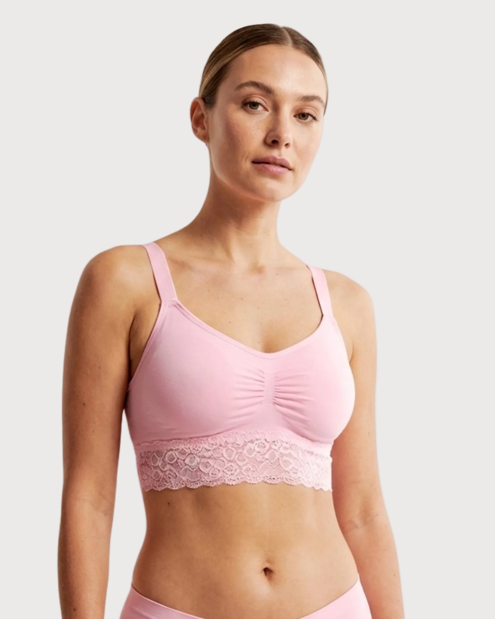 Woman wearing a pink Seamless Bra with lace Band with lace trim on a plain background