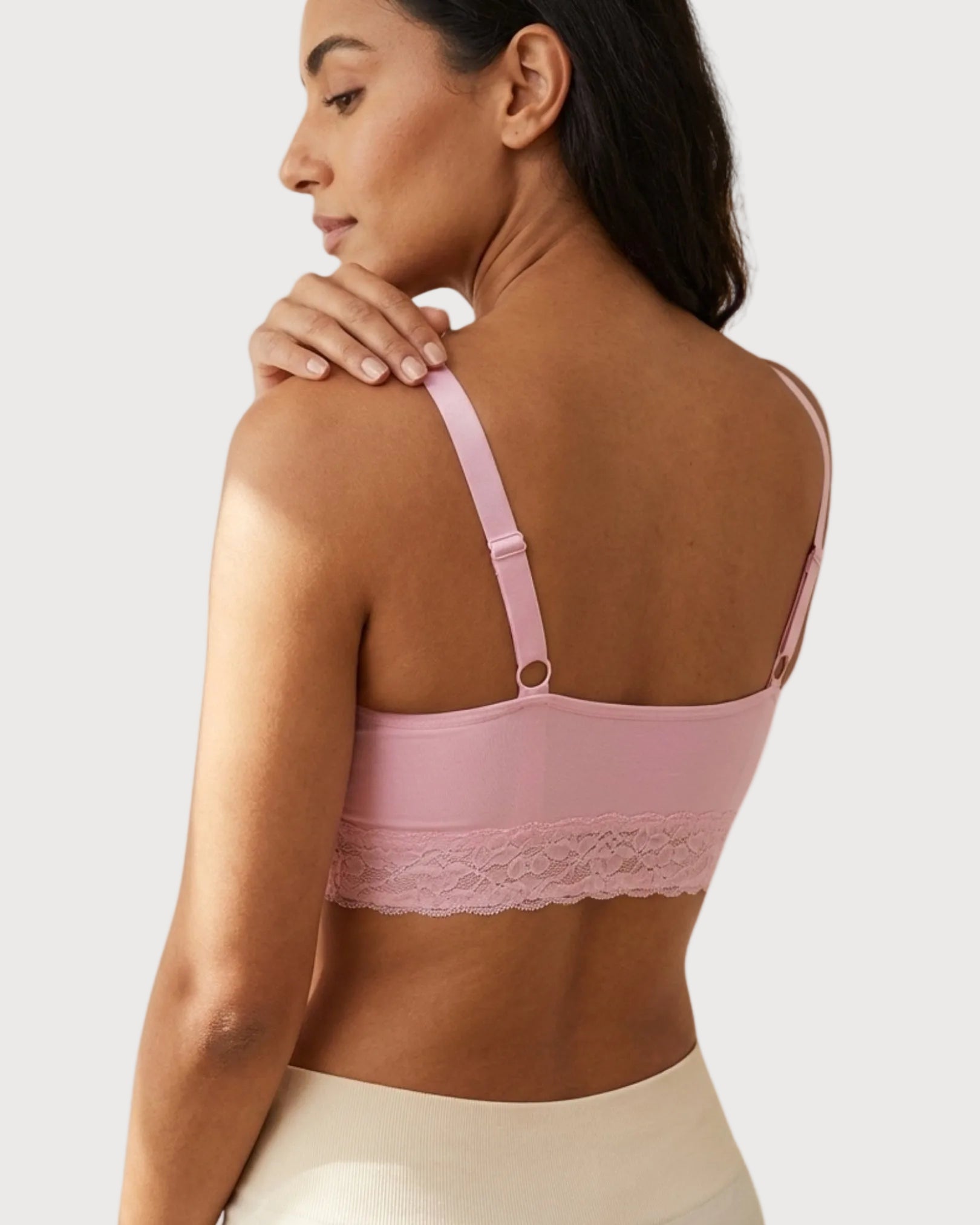 Back view of a woman wearing a pink Seamless Bra with lace Band with lace trim on a plain background