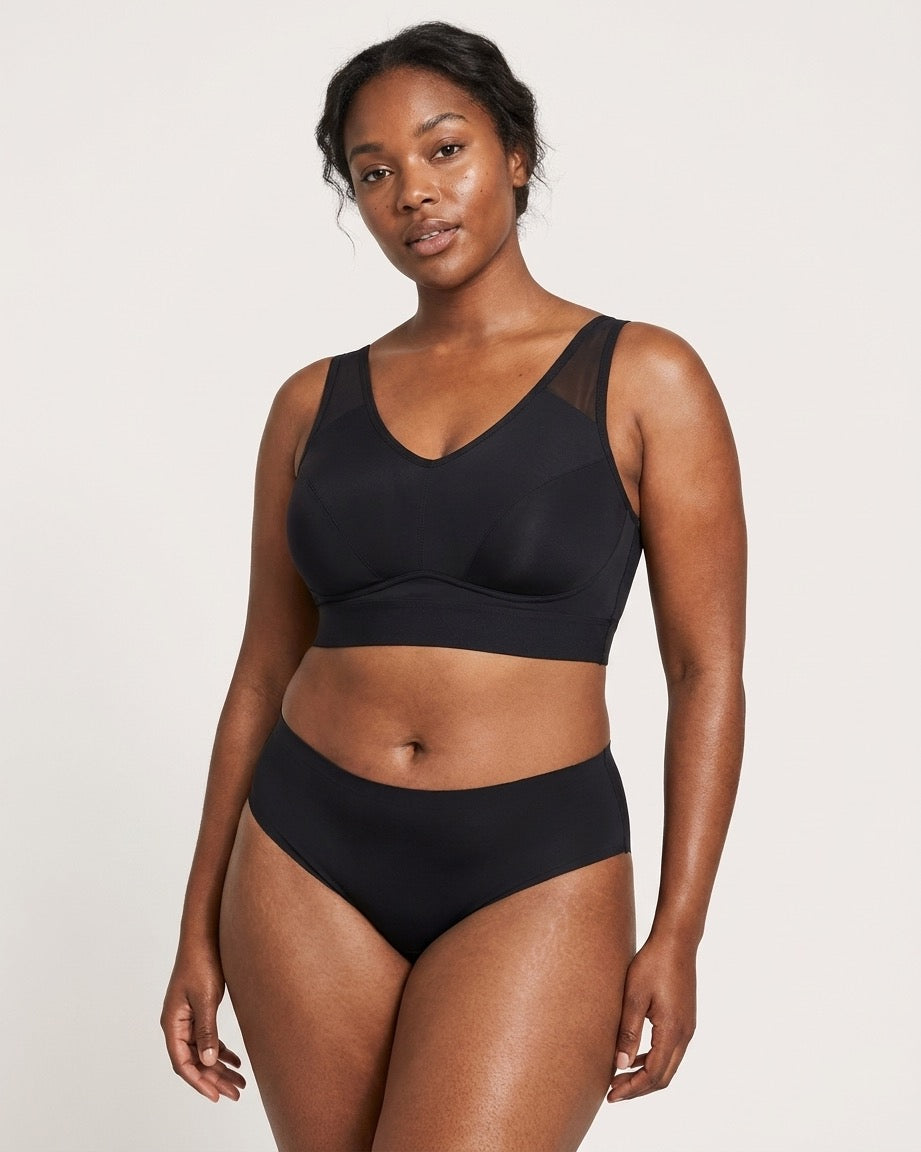 A woman modeling a black Mesh Front Leisure Bra, against a plain light gray studio background.