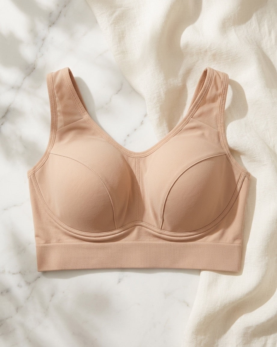 A Mesh Front Leisure Bra in a beige color, laid flat on a white marble surface with soft white fabric draped around it.