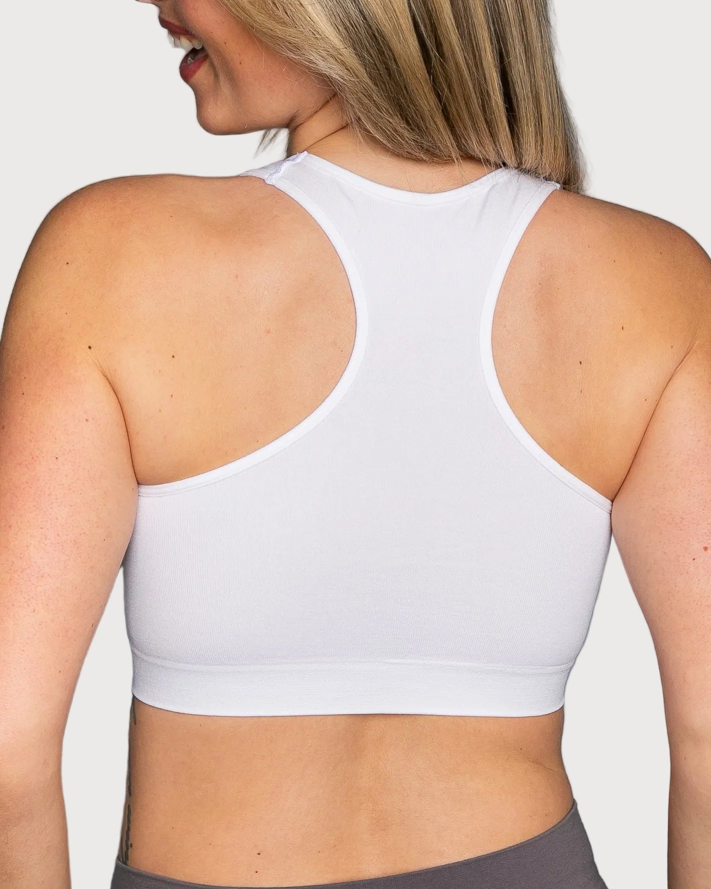 A woman shown from the back wearing a white Seamless Racerback Ahh Bra against a light gray studio background.