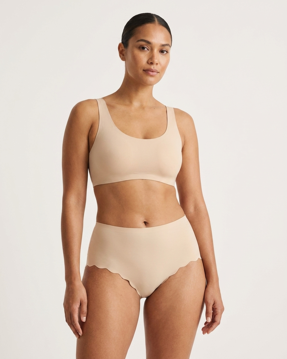 Woman wearing beige Invisible Edge Scalloped Briefs against a plain background