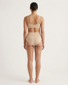 Backside of a woman wearing beige Invisible Edge Scalloped Briefs against a plain background