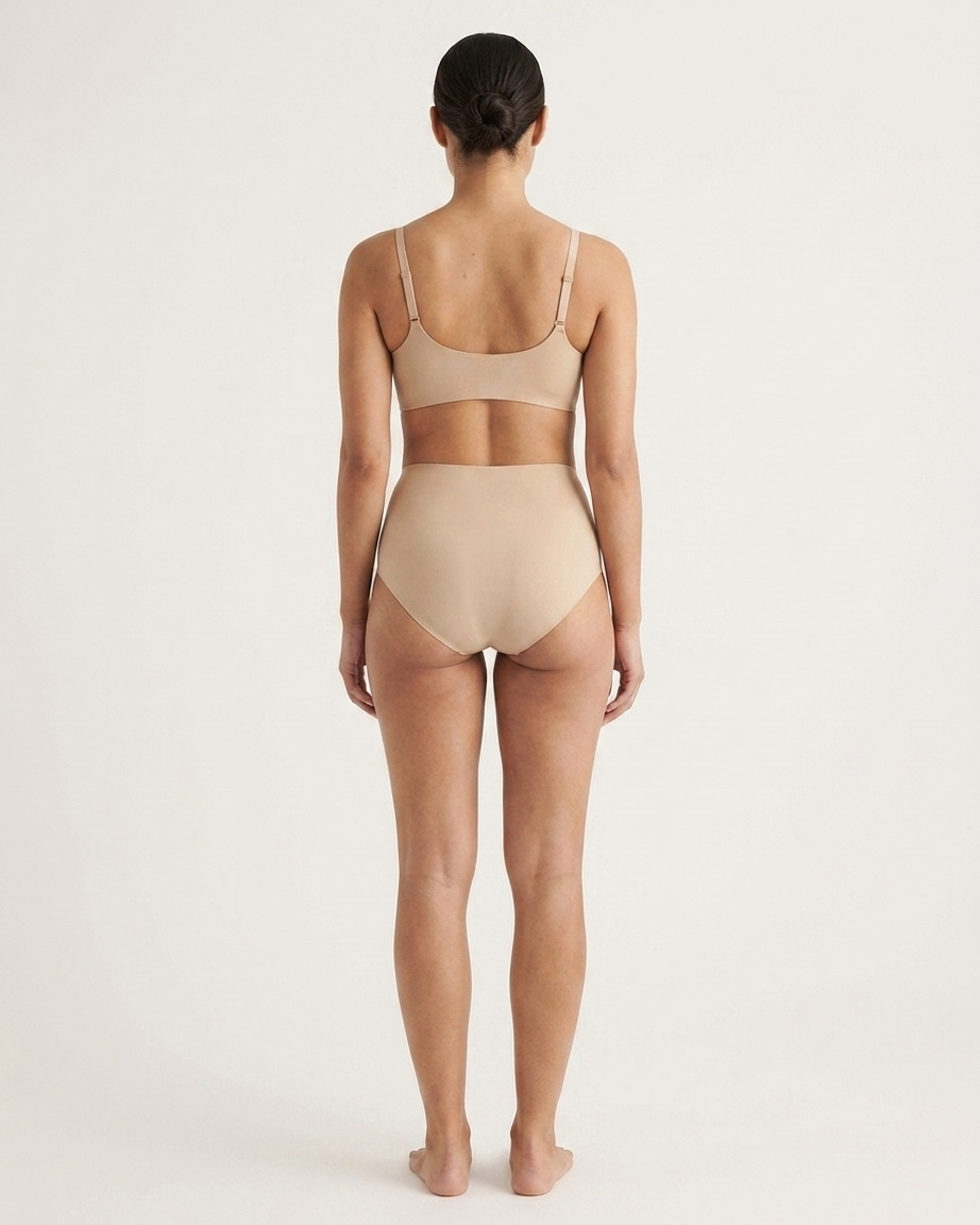 Backside of a woman wearing beige Invisible Edge Scalloped Briefs against a plain background