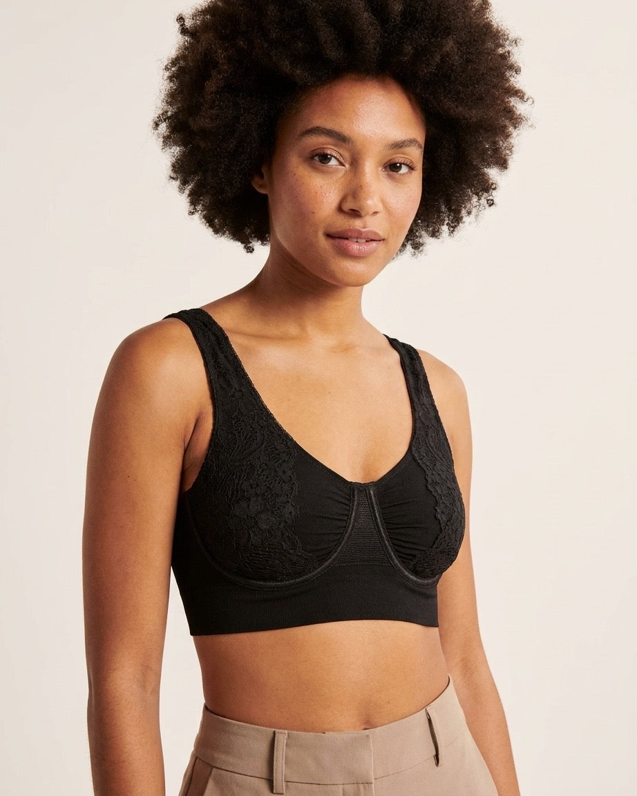 A woman wearing a black Seamless UW Bra w/ Lace Sling, photographed against a solid light beige background.