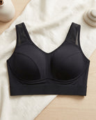 A black Mesh Front Leisure Bra, laid flat on a cream fabric surface with a light wood background and small decorative props.