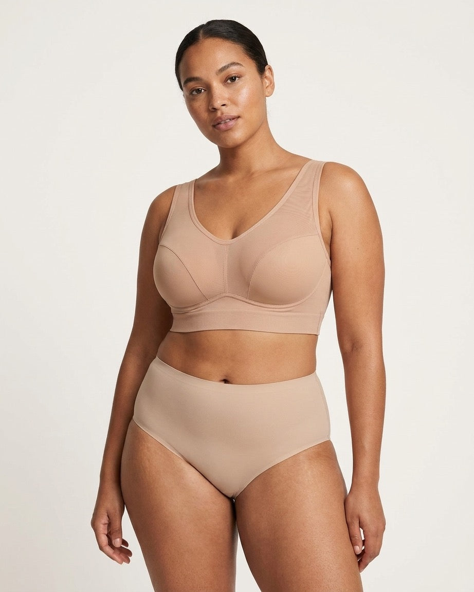 A woman modeling a beige Mesh Front Leisure Bra, photographed against a clean light gray studio background.